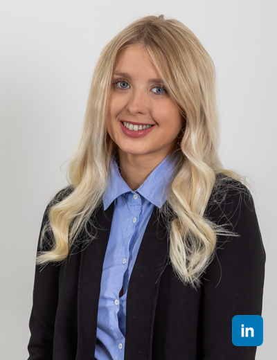 A profile image of a smiling white woman with long light blonde hair in waves. She has natural make up and wears a blue buttoned shirt with a black blazer.