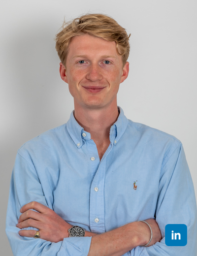 A profile image of a smiling blonde man with a light blue buttoned shirt. His blonde hair is tousled and side parted and his arms are folded.