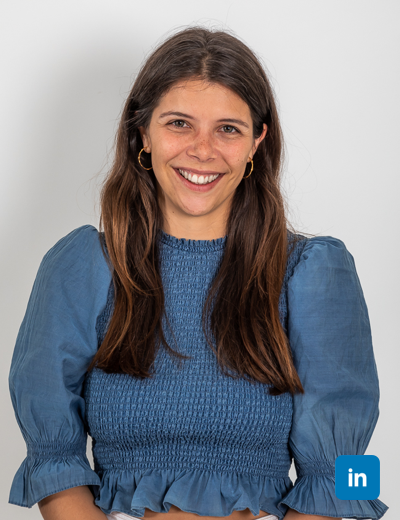 A profile image of a smiling white woman with long brown straight hair. She wears a blue top with frill trim