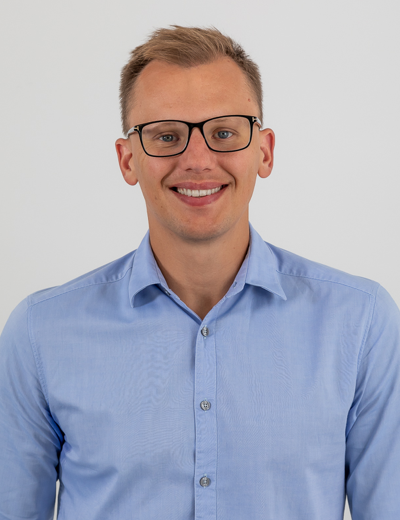 A profile photo of a young blonde white man with dark rimmed glassed and a blue buttoned shirt.
